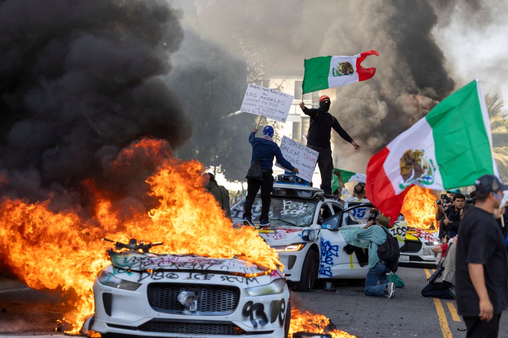 Protesters collide with law enforcement, igniting cars during an immigration protest in Los Angeles.